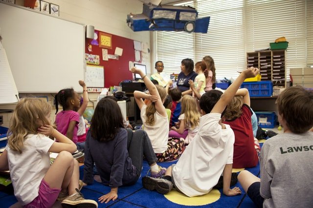 Students raising hands in a school classroom.